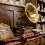 Gramophone ancien avec pavillon en laiton ornementé posé dans une boutique d'antiquités, entouré de disques en shellac et de mobilier ancien