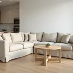Canapé d'angle recouvert d'une housse en lin beige dans un salon moderne et lumineux avec parquet en chêne clair