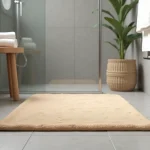 Tapis antidérapant en microfibre beige posé devant une douche italienne aux carreaux gris clair dans une salle de bains minimaliste