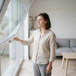 Femme ouvrant une fenêtre pour ventiler un appartement bien isolé en été afin de gérer la chaleur sans climatisation