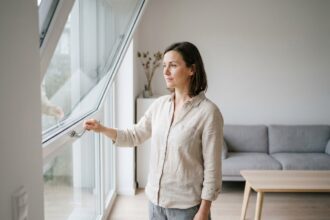 Femme ouvrant une fenêtre pour ventiler un appartement bien isolé en été afin de gérer la chaleur sans climatisation